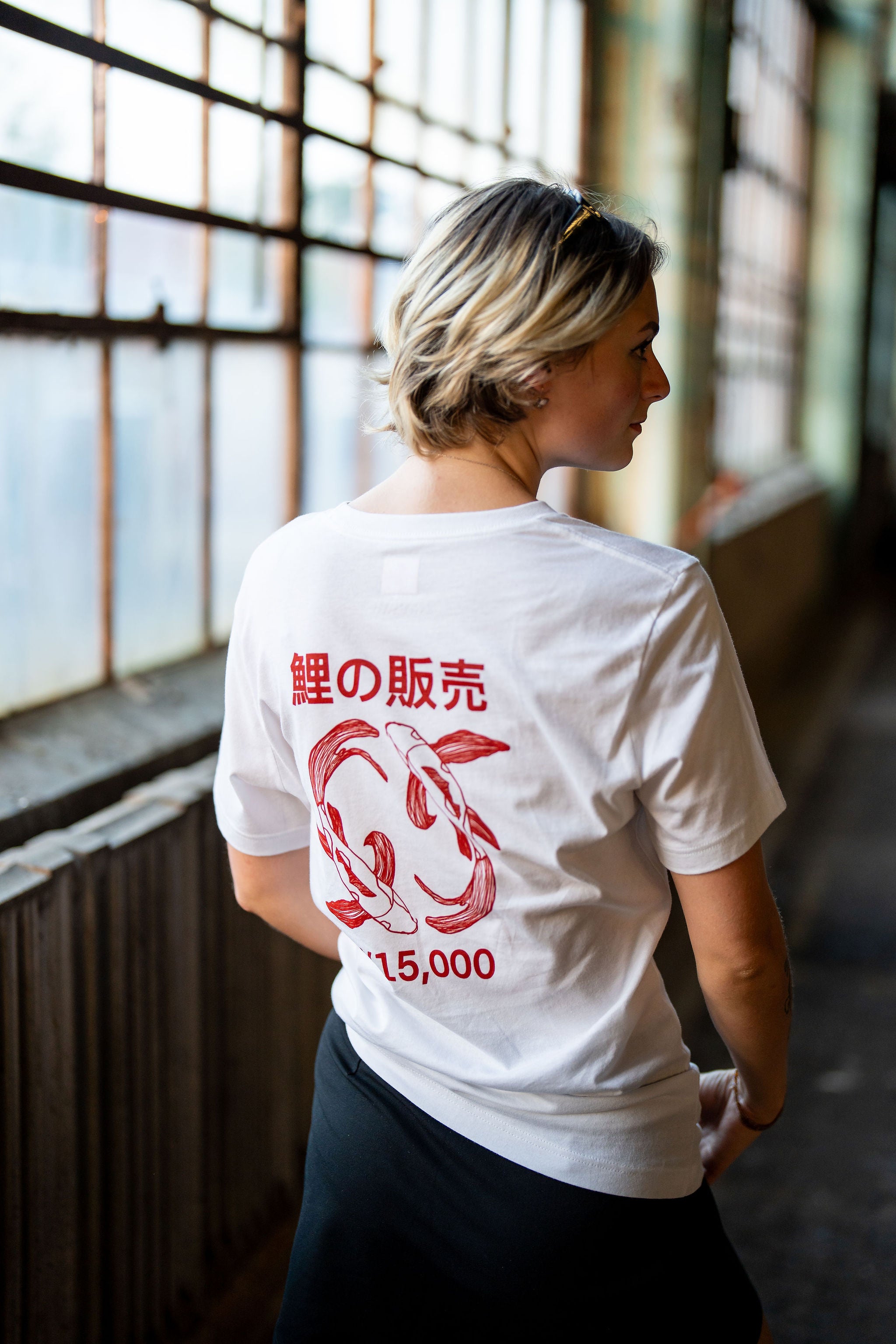Woman wearing white streetwear shirt with a koi fish design in red on the back